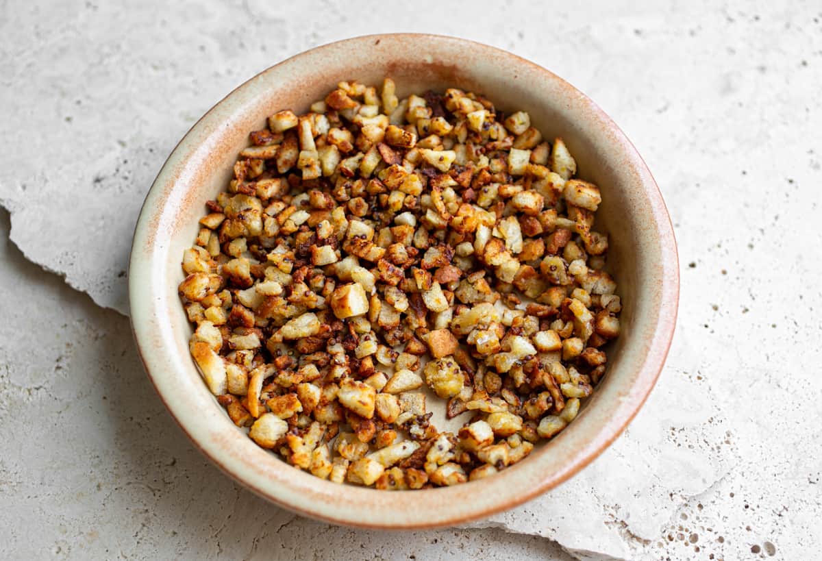 beige cermaic bowl on a beige ceramic table filled with crunchy mustard parmesan croutons